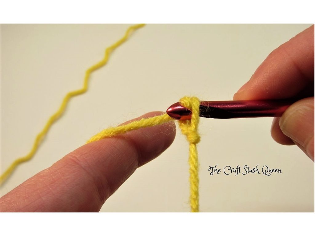 Yellow yarn on crochet hook.  Demonstrating how to make a chain stitch by pulling yarn through loop.