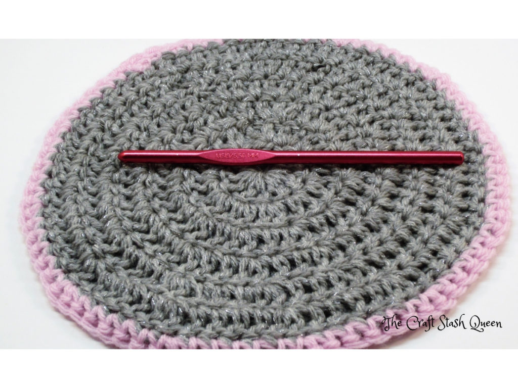 Size I-9 crochet hook on gray and pink crocheted doily.