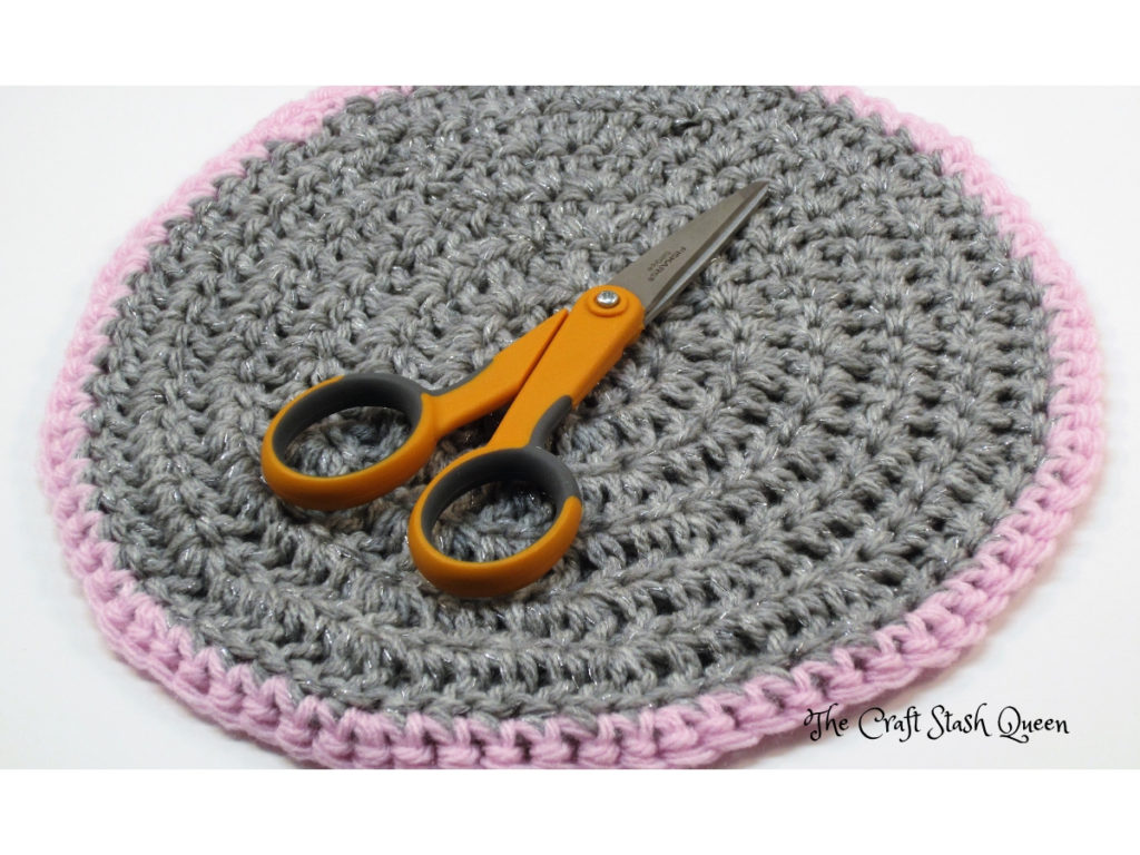 Small orange handle scissors on gray and pink crochet doily.