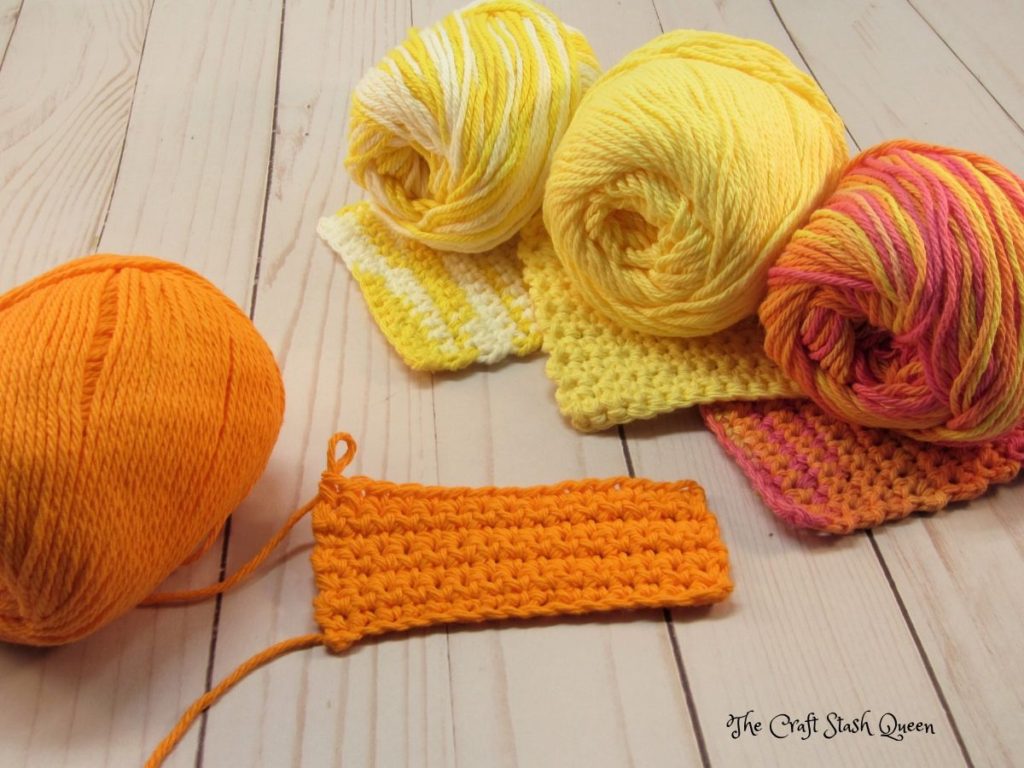 Cotton yarn skeins in orange, yellow ombre, yellow, orange ombre.  Three completed absolute beginner crochet coasters.  One in progress.