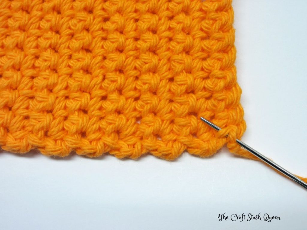 Completed absolute beginner crochet coaster pattern in orange cotton yarn.  Darning needle demonstrating first step of weaving in ends.