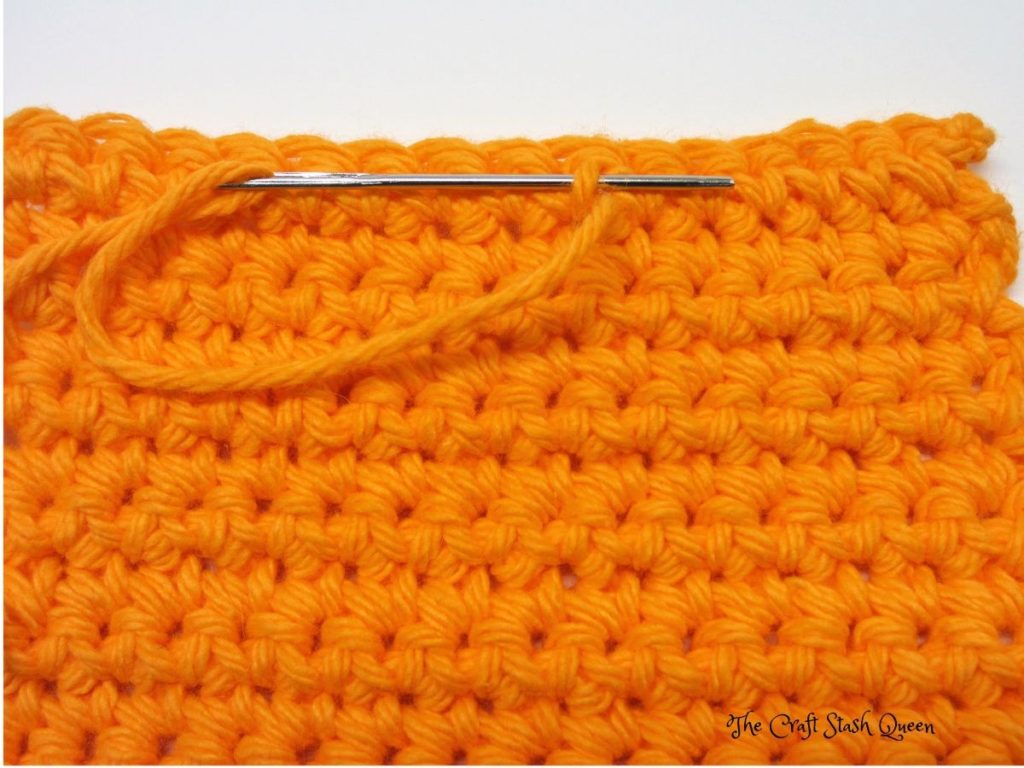 Completed absolute beginner crochet coaster pattern in orange cotton yarn.  Darning needle demonstrating third step of weaving in ends.