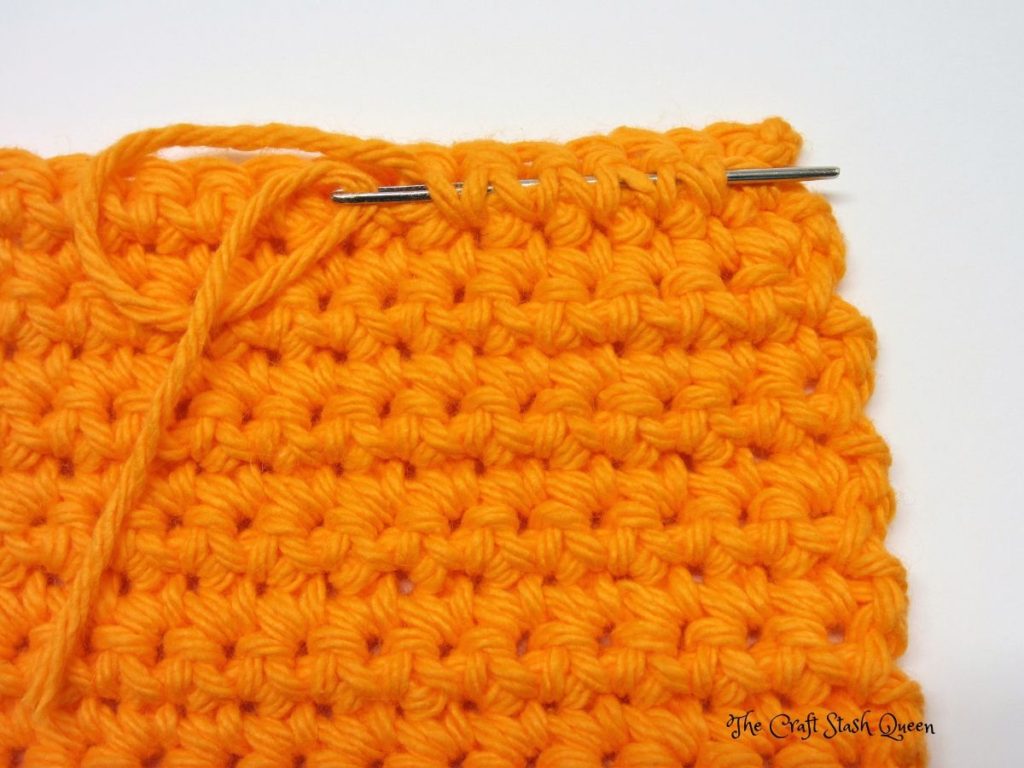 Completed absolute beginner crochet coaster pattern in orange cotton yarn.  Darning needle demonstrating last step of weaving in ends.