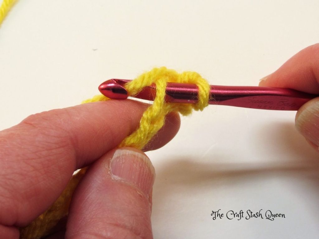 Red crochet hook with active loop on hook.  Hook is inserted into second chain from hook. Yarn is wrapped around hook from back to front.