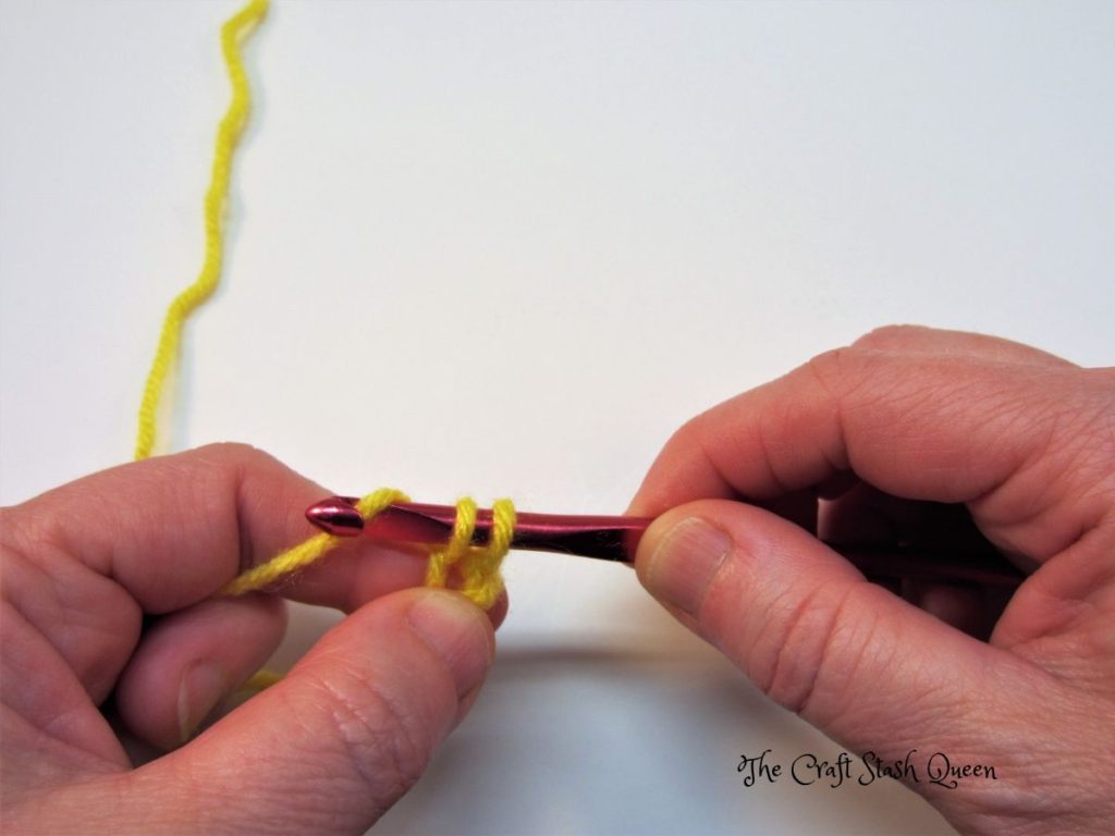 Yellow yarn.  Red crochet hook with two loops on the hook and a yarn over being demonstrated.