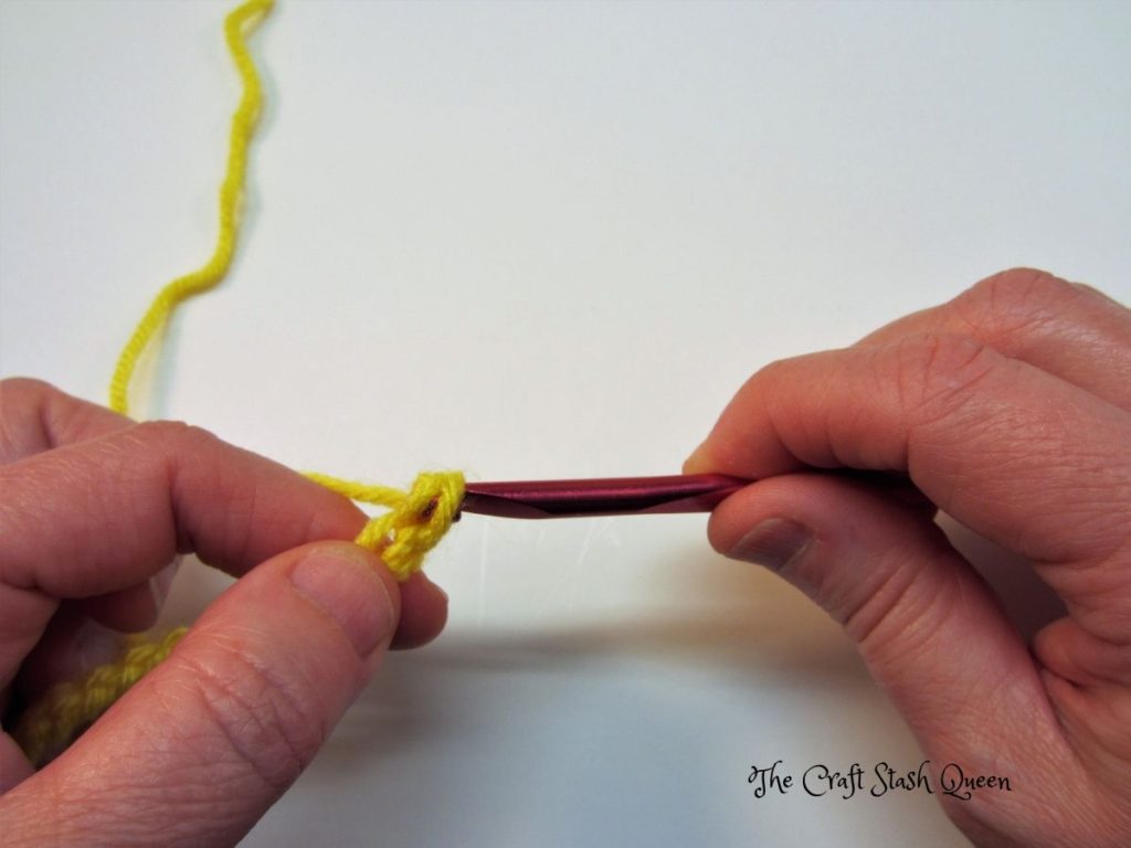 Red crochet hook with yellow yarn.  Demonstrating pulling through 2 loops on crochet hook.