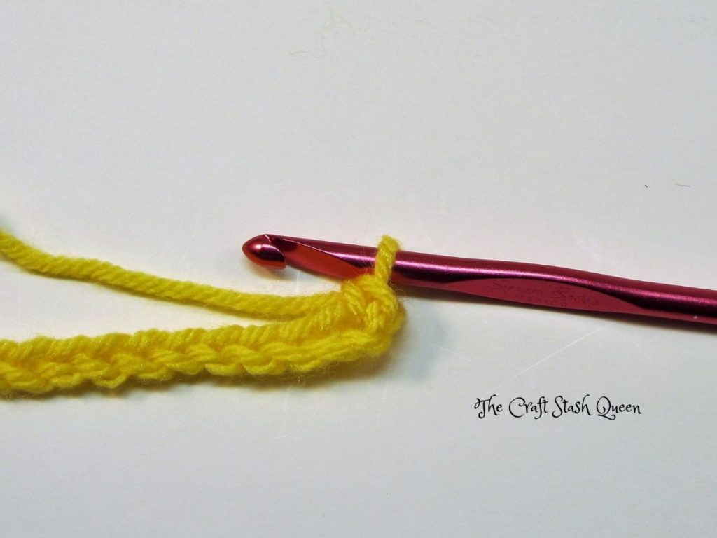 Red crochet hook.  Yellow yarn crocheted into a chain with one single crochet.