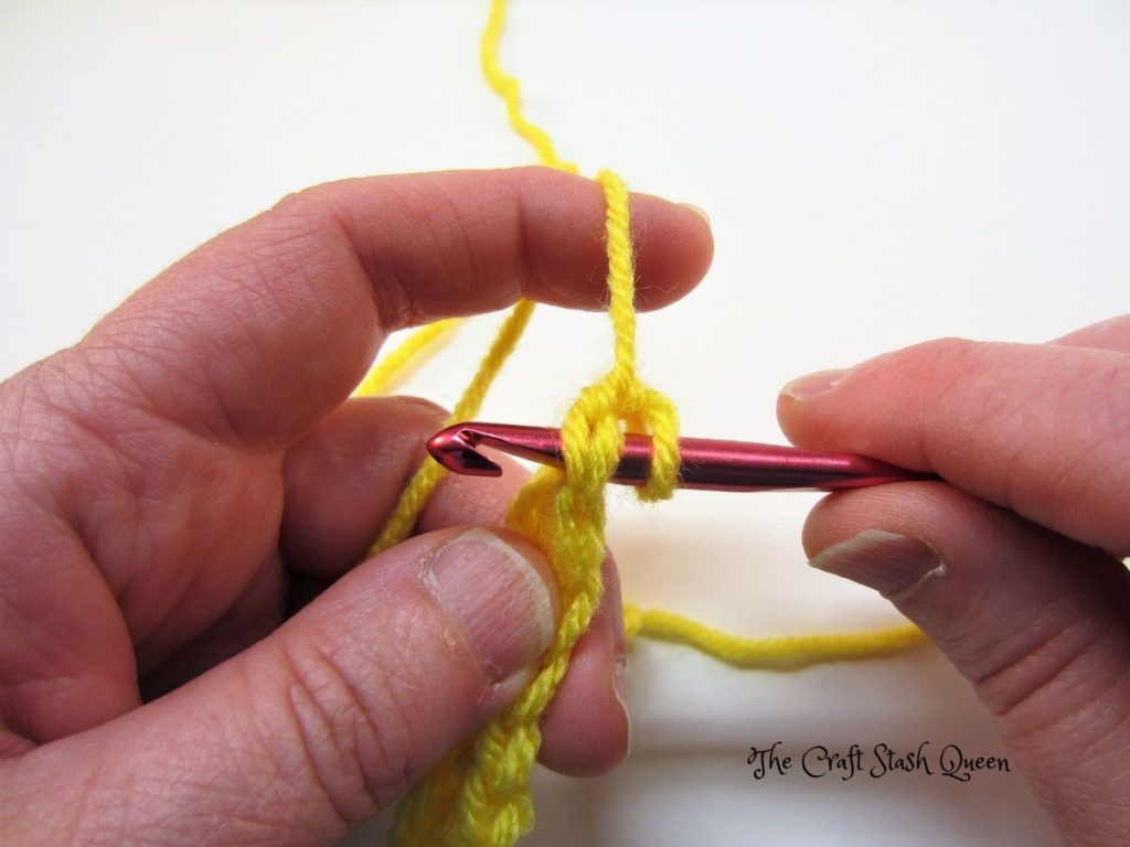 Red crochet hook inserted into top of single crochet.  Yellow yarn.